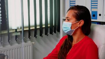 Portrait of woman with protection mask looking and working on computer. Employee in new normal office workspace typing on computer keyboard looking at desktop respecting social distancing video