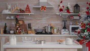 Empty christmas decorated culinary kitchen with nobody in it ready for traditional festive holiday. On table standing homemade cookie dessert ingredients with glass of milk, strainer video