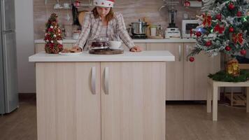 Portrait of girl wearing santa hat looking into camera standing at table in xmas decorated kitchen. Children enjoying winter holidays celebrating christmas. Baked traditional cookies video