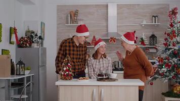 avós dando embrulho natal presente presente com fita em isto para neto em pé às mesa dentro decorado cozinha. feliz família desfrutando inverno estação a comemorar Natal feriado video