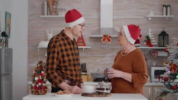 contento nieta sorprendente abuelos con envoltura presente con cinta en eso celebrando tiempo de Navidad. familia disfrutando invierno fiesta en Navidad decorado cocina durante Navidad temporada video