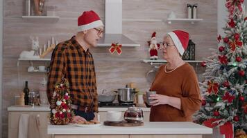 grootouders met kleinkind vervelend de kerstman hoed groet afgelegen vrienden gedurende online video-oproep vergadering staand Bij tafel in Kerstmis versierd culinaire keuken. gelukkig familie genieten van Kerstmis vakantie video