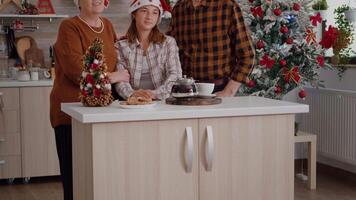 Portrait of grandparents with granddaughter spending winter holiday together standing at table in xmas decorated kitchen. Happy family wearing santa hat celebrating christmas season video