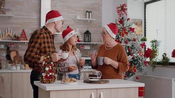 barn diskuterar med farföräldrar äter bakad hemlagad utsökt småkakor njuter jultid. familj bär santa hatt skrattande medan fira jul festlig Semester i dekorerad kök video