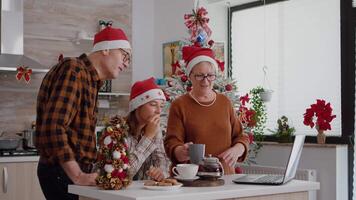 família falando com controlo remoto pais durante conectados Video chamada encontro em computador portátil a comemorar inverno festivo estação junto. avós família desfrutando Natal feriado dentro decorado cozinha