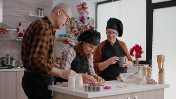 Grandparents teaching granddaughter how to make xmas homemade gingerbread using cookies shape in decorated culinary kitchen. Happy family spending time together during christmas holiday video