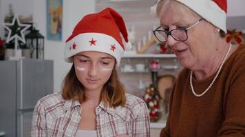 Grandmother teaching granddaughter how sift flour ingredient preparing homemade delicious dessert. Happy family wearing santa hat enjoying baking traditional cookie celebrating christmas video