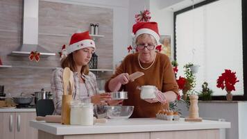 neta usando cozinha filtro enquanto avó colocando farinha ingrediente preparando caseiro tradicional sobremesa desfrutando cozinhando junto. feliz família a comemorar Natal feriados video