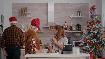 abuela acecho Navidad en línea con nieta en tableta mientras abuelo trayendo Leche disfrutando tradicional festivo estación. contento familia celebrando Navidad fiesta en decorado cocina video