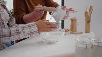 Closeup of grandmother hands putting flour in strainer while granddaughter sift ingredient in kitchen bowl preparing xmas homemade cookie dessert. Family celebrating christmas enjoying winter holiday video