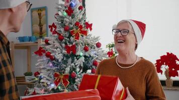 feliz Senior casal desfrutando época de Natal partilha embrulho presente presente dentro natal decorado cozinha às lar. animado família com santa chapéu desfrutando Natal feriado durante inverno estação video