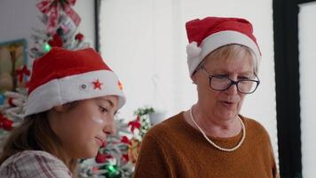 Porträt von Oma mit Enkelin tragen Santa Hüte Kochen im Weihnachten dekoriert kulinarisch Küche. glücklich Familie genießen Backen köstlich Dessert Sichtung Mehl während Weihnachten Ferien video