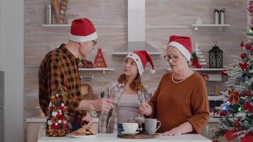 grand-père portion enfant avec cuit délicieux biscuit tandis que grand-mère en mettant café profiter dépenses ensemble période de Noël saison. famille permanent dans décoré cuisine pendant Noël vacances video