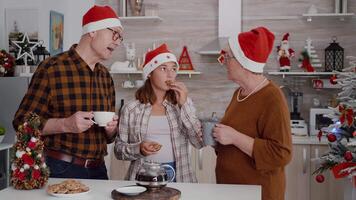 Happy family celebrating christmas holiday enjoying spending winter season together in xmas decorated culinary kitchen. Grandchild eating baked delicious cookies while grandparents drinking coffee video