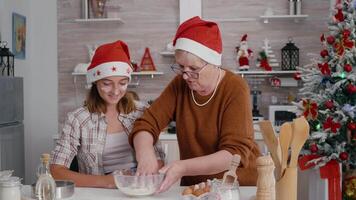 Gradma with granddaughter mixing ingredients egg with flour preparing homemade traditional dough making xmas delicious dessert. Happy family enjoying cooking during christmas holidays video