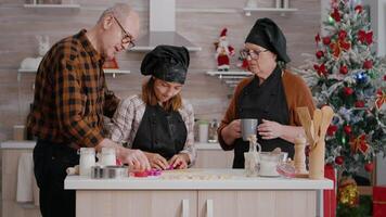 nipote mostrando per nonni Come utilizzando biscotti forma preparazione tradizionale fatti in casa Pan di zenzero nel culinario cucina. contento famiglia godendo la spesa Natale vacanza insieme video