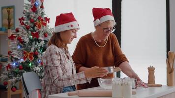 Grandmother putting flour ingredients in strainer explaining to granddaughter how to prepare traditional homemade cookie dessert in christmas decorated kitchen. Family enjoying winter holiday video