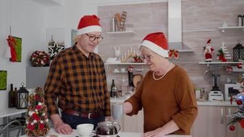 Happy family with santa hat greeting remote friends during online videocall meeting using phone celebrating christmas holiday together. Granddaughter enjoying winter season in xmas decorated kitchen video