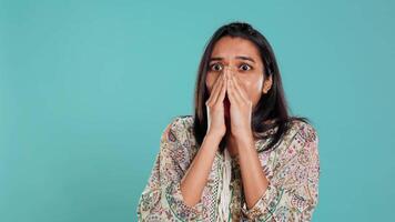 anxieux Indien femme couvrant visage avec palmiers, inquiet à propos avenir, isolé plus de studio Contexte. tendu la personne sous le choc par troublant nouvelles, halètement, sentiment affligé, caméra b video