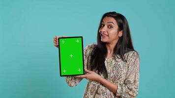 Person doing influencer marketing using isolated screen tablet, studio background. Indian woman holding empty copy space chroma key digital device, doing review, camera A video