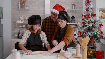 Grandparents teaching granddaughter how prepare homemade gingerbread dough using traditional rolling pin celebrating christmas holidays in xmas decorated kitchen. Happy family making delicious cookies video