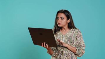 irritado mujer luchando con compañeros de trabajo durante videollamada en computadora portátil, aislado terminado estudio antecedentes. indignado persona discutiendo con colegas durante conversacion en computadora portátil, cámara un video