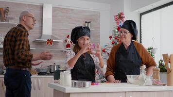 Granddaughter with apron cooking in culinary kitchen using xmas cookies shape preparing delicious gingerbread dessert. Happy family enjoying winter season celebrating christmas holiday video