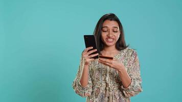 Woman adding payment method on shopping website using phone, taking advantage of promotions, studio background. Indian person buying stuff online using credit card, typing data on device, camera A video