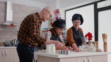 abuelos disfrutando gasto hora con nieta Cocinando pan de jengibre postre haciendo galletas forma utilizando tradicional hecho en casa masa. contento familia celebrando Navidad fiesta video