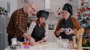 Grandparents teaching granddaughter how prepare gingerbread dessert shape using traditional homemade cookies dough. Happy family enjoying winter holiday celebrating christmas in culinary kitchen video