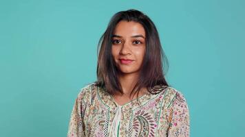 Portrait of cheerful friendly indian woman smiling, looking pleased, isolated over studio background. Happy person in traditional attire having positive facial expression, feeling satisfied, camera B video