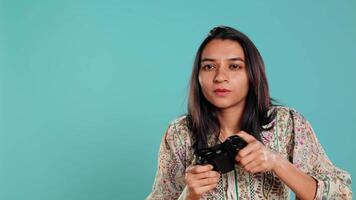 Cheerful indian gamer showing thumbs up sign gesturing while holding controller after winning videogame. Joyful woman enjoying games, doing approving hand gesture, studio background, camera B video