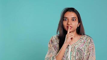 Annoyed indian woman doing shushing hand gesturing, irritated by noise, having negative mood. Person placing finger on lips, doing quiet sign gesture, isolated over studio background, camera B video