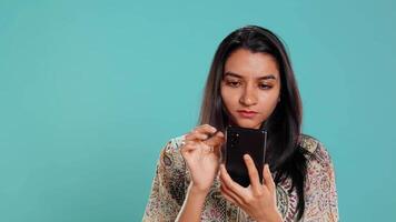 Indisch vrouw vegen Aan smartphone touch screen naar antwoord telefoon telefoontje van vriend, geïsoleerd over- studio achtergrond. portret van persoon luisteren en akkoord gaan met maat gedurende telefoon telefoongesprek, camera b video