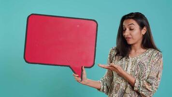 souriant Indien femme en portant rouge discours bulle signe de vide copie espace pour message. joyeux la personne en présentant pensée bulle papier carton utilisé comme promotion concept, studio arrière-plan, caméra une video