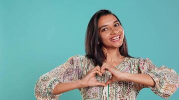 retrato de sonriente amoroso mujer haciendo corazón símbolo forma gesto con manos, demostración amabilidad. contento cariñoso Novia haciendo oferta amor gesticulando para novio, estudio fondo, cámara si video