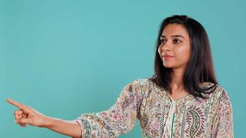 Salesman pointing around with finger, doing recommendation, talking with audience. Indian woman showing copy text space, doing advertisement, isolated over studio background, camera B video