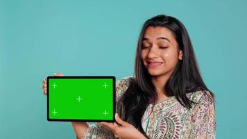 Energetic salesman doing influencer marketing using green screen tablet, studio background. Lively woman reviewing product, holding empty copy space mockup digital device, camera B video