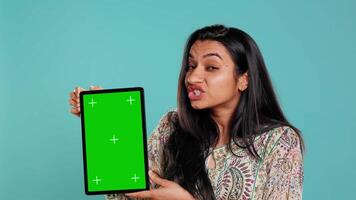 Person doing influencer marketing using isolated screen tablet, studio background. Indian woman holding empty copy space chroma key digital device, doing review, camera B video