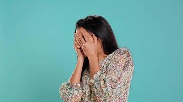 Fearful indian woman covering face with palms, worried about troubling peril, isolated over studio background. Insecure person fearing endangerment, feeling distressed in face of adversity, camera B video