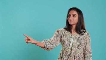 Salesman pointing around with finger, doing recommendation, talking with audience. Indian woman showing copy text space, doing advertisement, isolated over studio background, camera A video