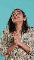 Vertical Indian woman putting hands together in begging gesture, making wish, isolated over studio background. Faithful person looking upwards to sky, asking for something, praying and hoping, camera A video