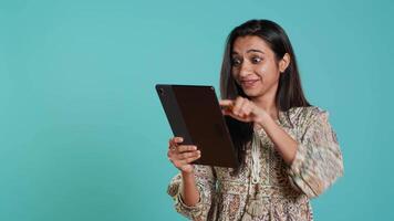 Joyous woman excited to purchase products, adding payment method on website, isolated over studio background. Happy customer does internet shopping, typing debit card info on tablet, camera A video