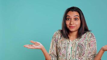 Indian woman shrugging shoulders, unable to provide answer, having detached apathy facial expression. Apathetic person doing hand gesturing showing lack of knowledge, studio background, camera B video