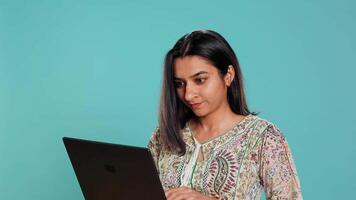 Indisch vrouw componeren e-mail, typen Aan laptop, gefrustreerd met defect toetsenbord. persoon Bezig met verzenden mail online, worstelen naar gebruik defecte notitieboekje, studio achtergrond, camera b video