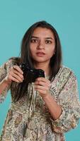 Vertical Competitive woman playing videogames with motion controlled controller, studio background. Indian Person participating in internet multiplayer racing game using gyroscope function on gamepad, camera A video