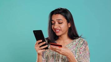 Woman adding payment method on shopping website using phone, taking advantage of promotions, studio background. Indian person buying stuff online using credit card, typing data on device, camera B video