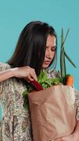 verticale dérangé femme renfrogné après oubli à acheter tout, à la recherche à l'intérieur papier sac avec des légumes. conscient vivant la personne bouder après réalisant certains les courses sont manquant, caméra une video