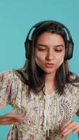 Vertical Happy woman playing electronic music and waving hand in air, pretending to use turntables. Cheerful DJ wearing headphones, producing beats, making songs, isolated over studio background, camera A video