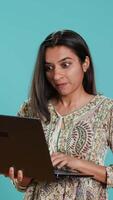 Vertical Indian woman composing email, typing on laptop, frustrated with malfunctioning keyboard. Person sending mail online, struggling to use defective notebook, studio background, camera A video